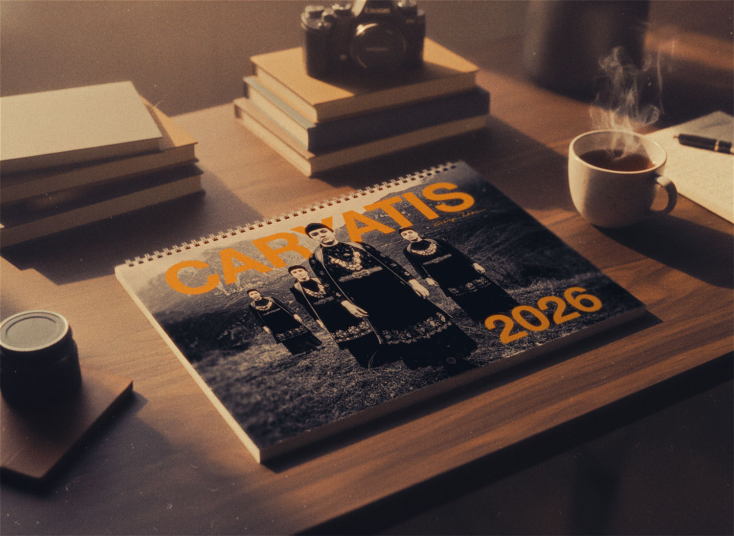 Calendar with 'CARATIS 2026' on a desk with books and a camera