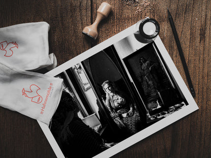 Woman looking at herself in a mirror in Soufli, Thrace, Greece, with a vintage photograph on the wall. Black and white photography print on table by George Tatakis