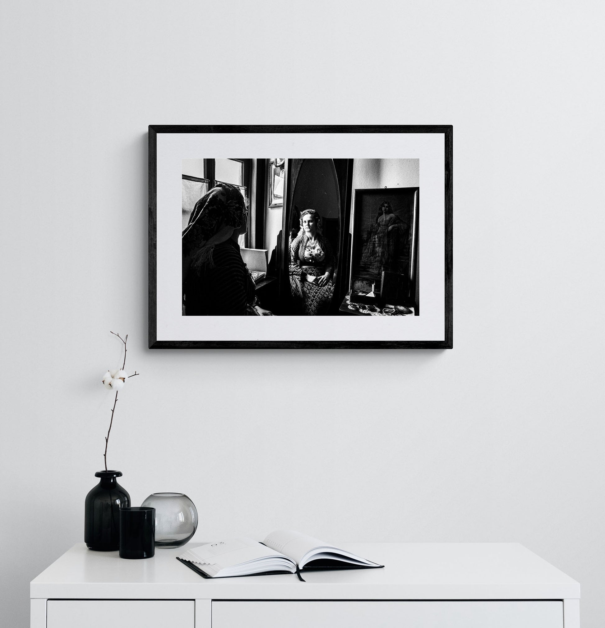 Woman looking at herself in a mirror in Soufli, Thrace, Greece, with a vintage photograph on the wall. Black and white photography framed on a wall by George Tatakis