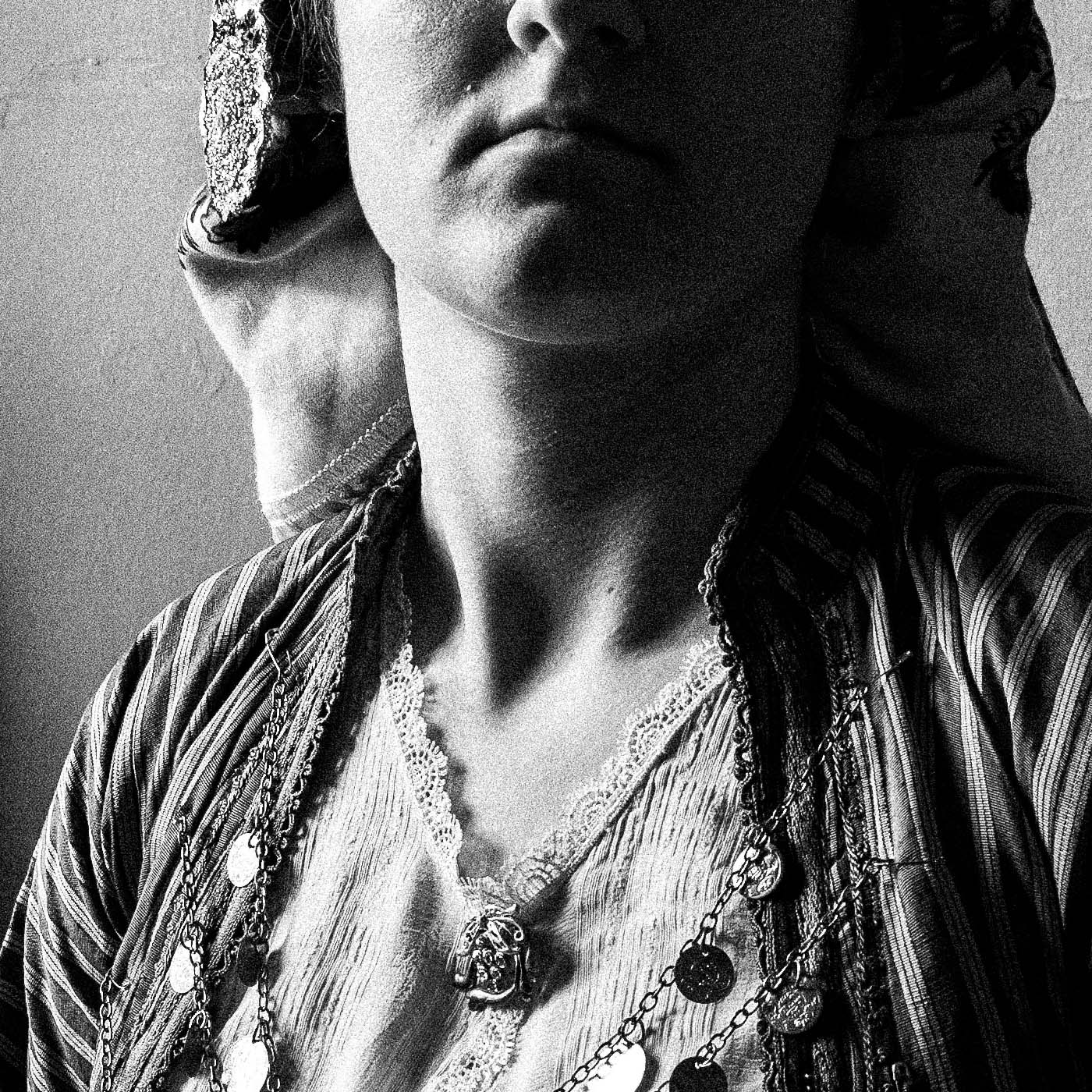 Black and white portrait of a woman in a room with framed pictures on the wall wearing the bridal dress of Soufli, Thrace, Greece. Photography close-up detail by George Tatakis