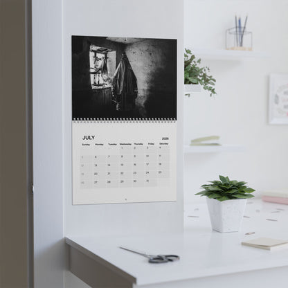Calendar on a wall with a black and white photo of a person hanging clothes, in a room with a desk and plant.