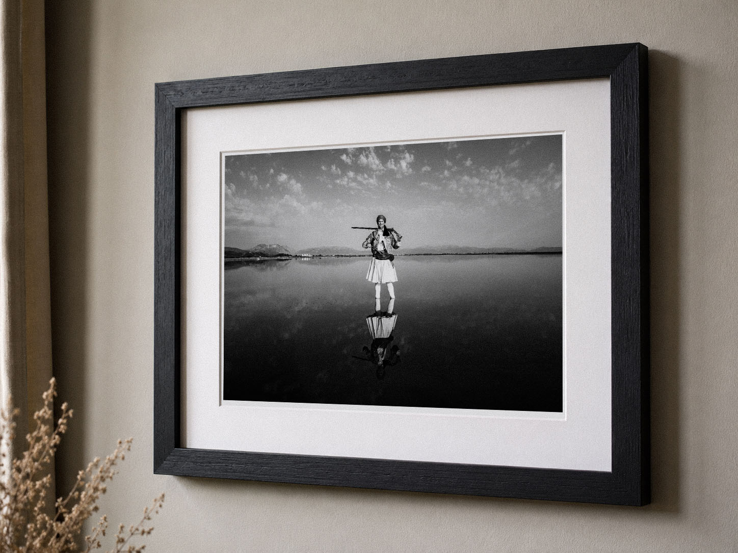 Framed black and white photograph of a person standing on water with a rifle, leaning against a wall.
