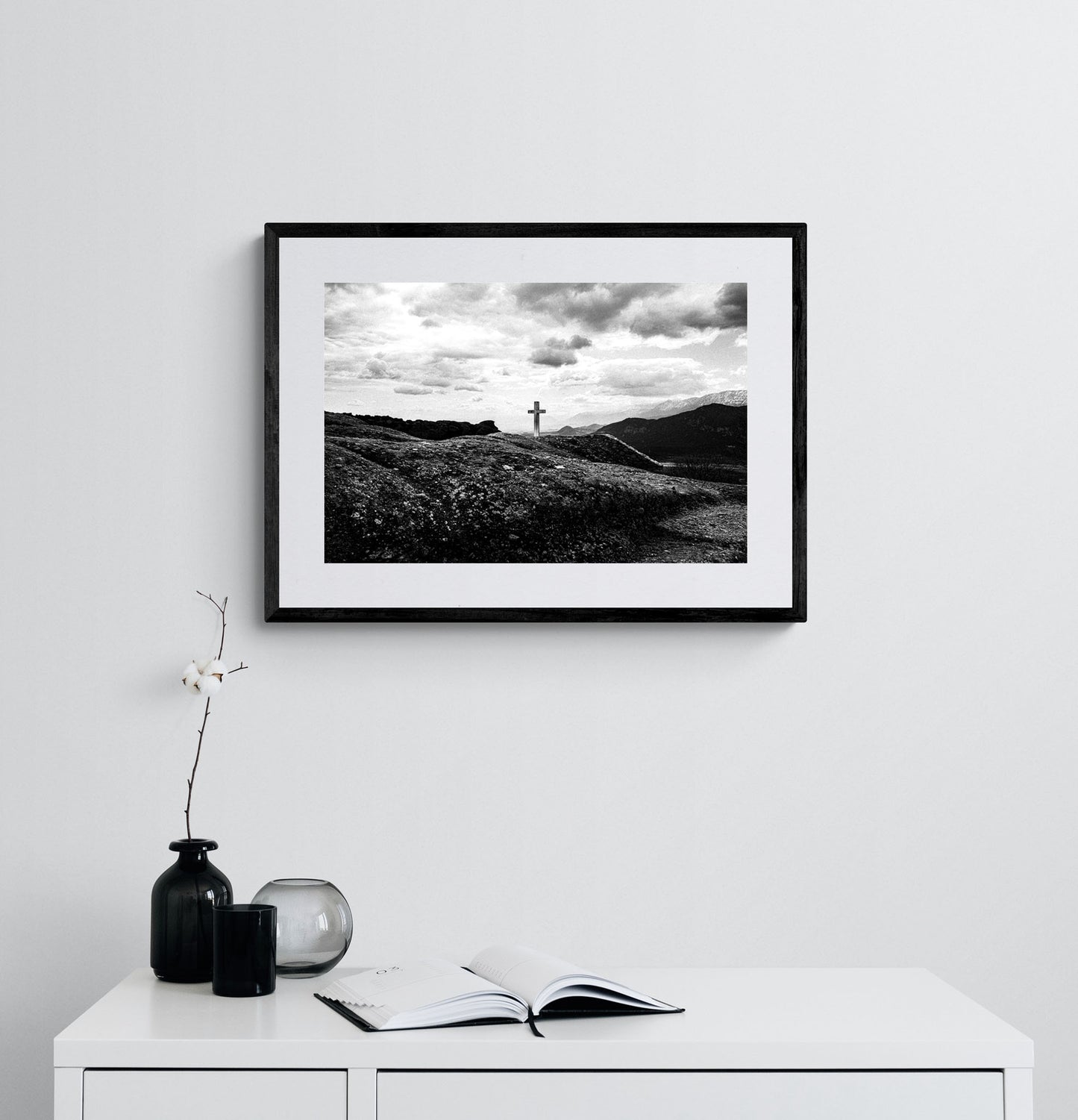 Cross on a rock at Meteora. Black-and-white photography artwork by George Tatakis from the project Chorōs. Framed on a white wall