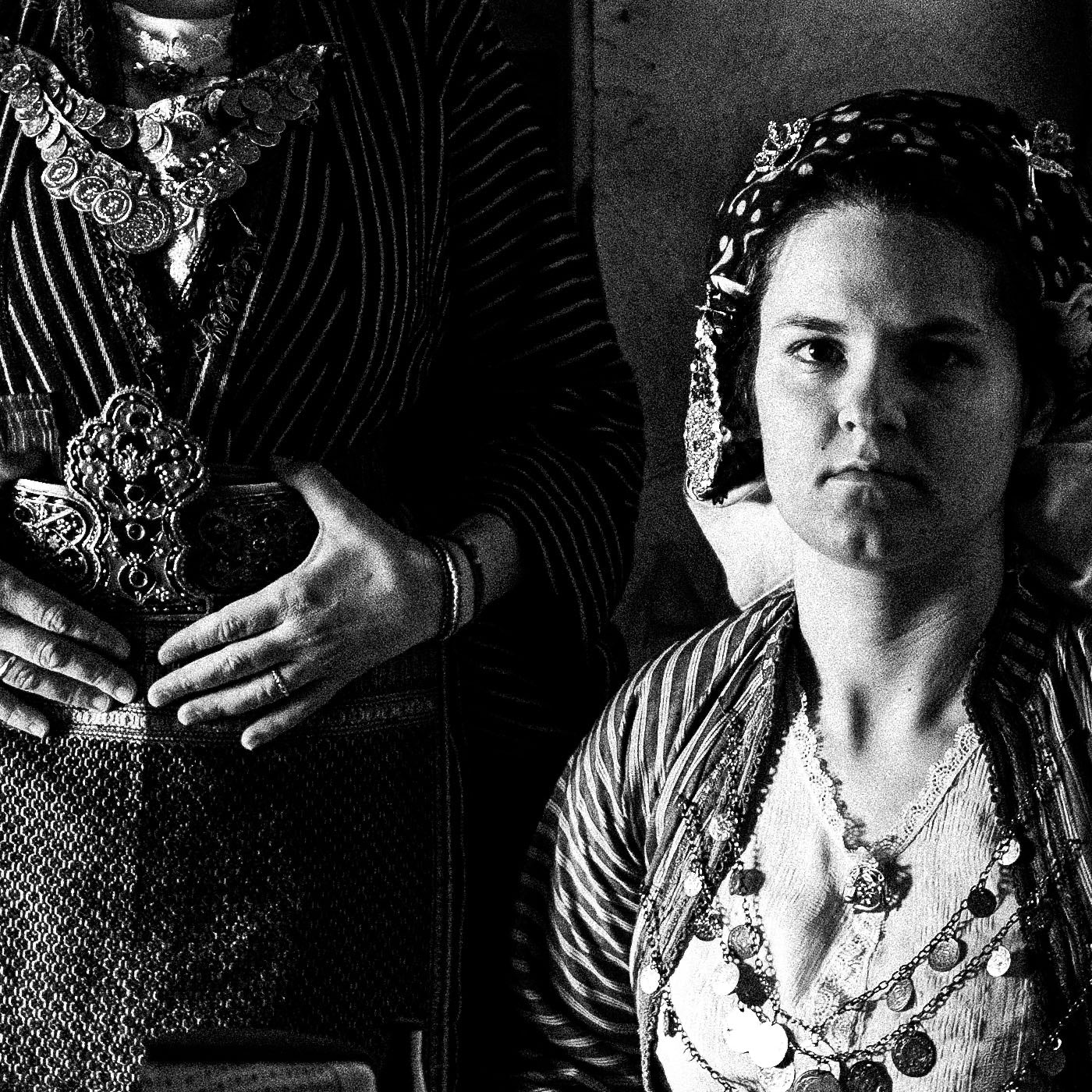 Three women in a room with shelves and shoes. Traditional costumes of Soufli, Thrace, Greece. Black and white photography close-up detail by George Tatakis