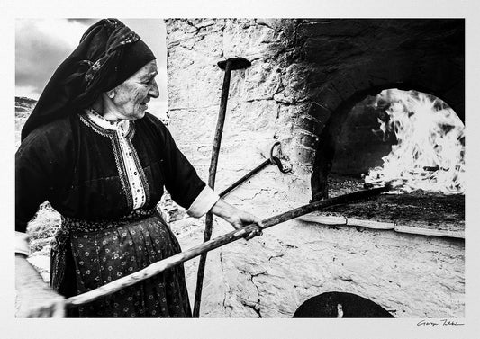 Black and White Photography Wall Art Greece | Woman spreading the fire inside wood oven in her traditional costume Olympos Karpathos by George Tatakis