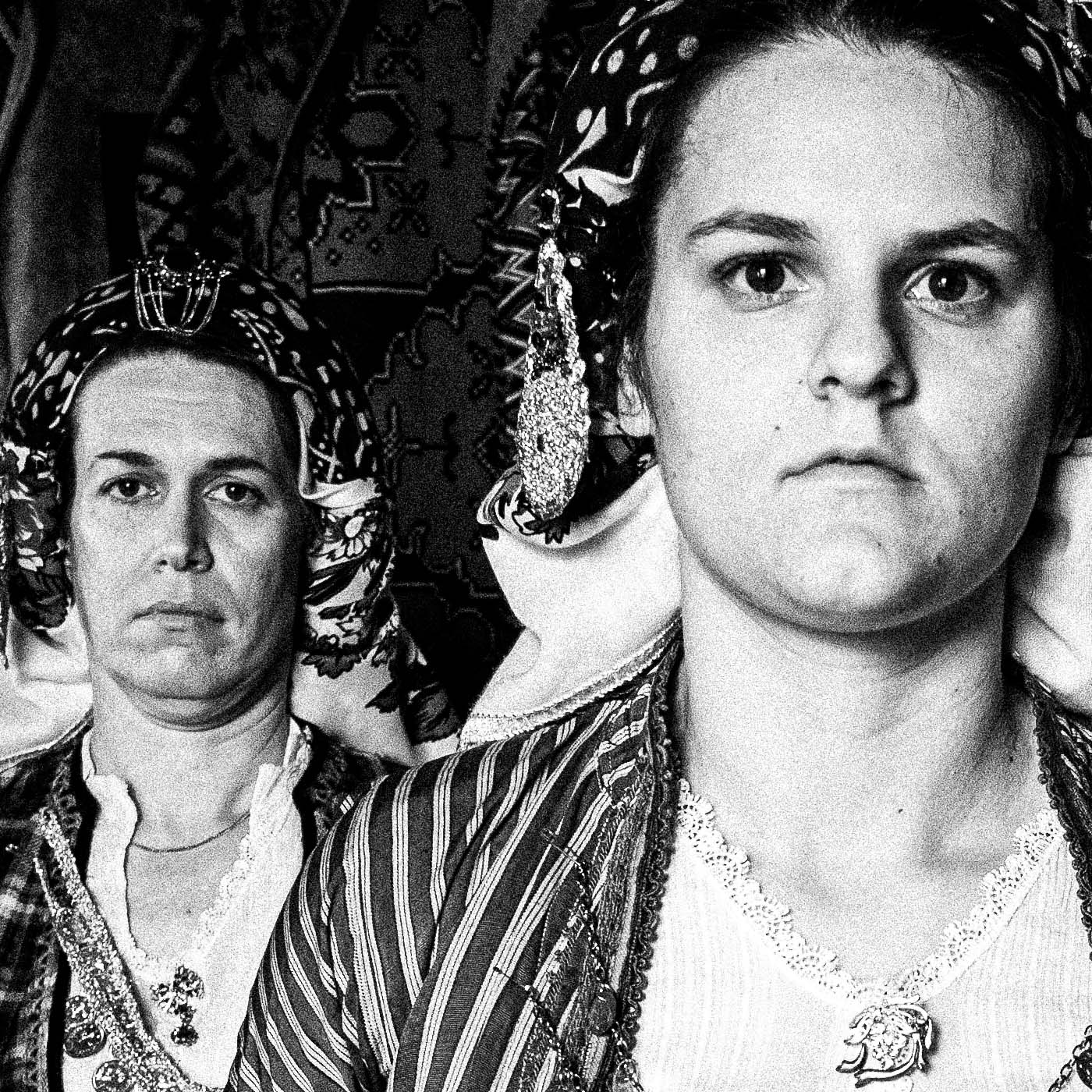 Black and white portrait of a woman in traditional attire with two other women in the background. Soufli local dresses, Thrace, Greece. Photography close-up detail by George Tatakis