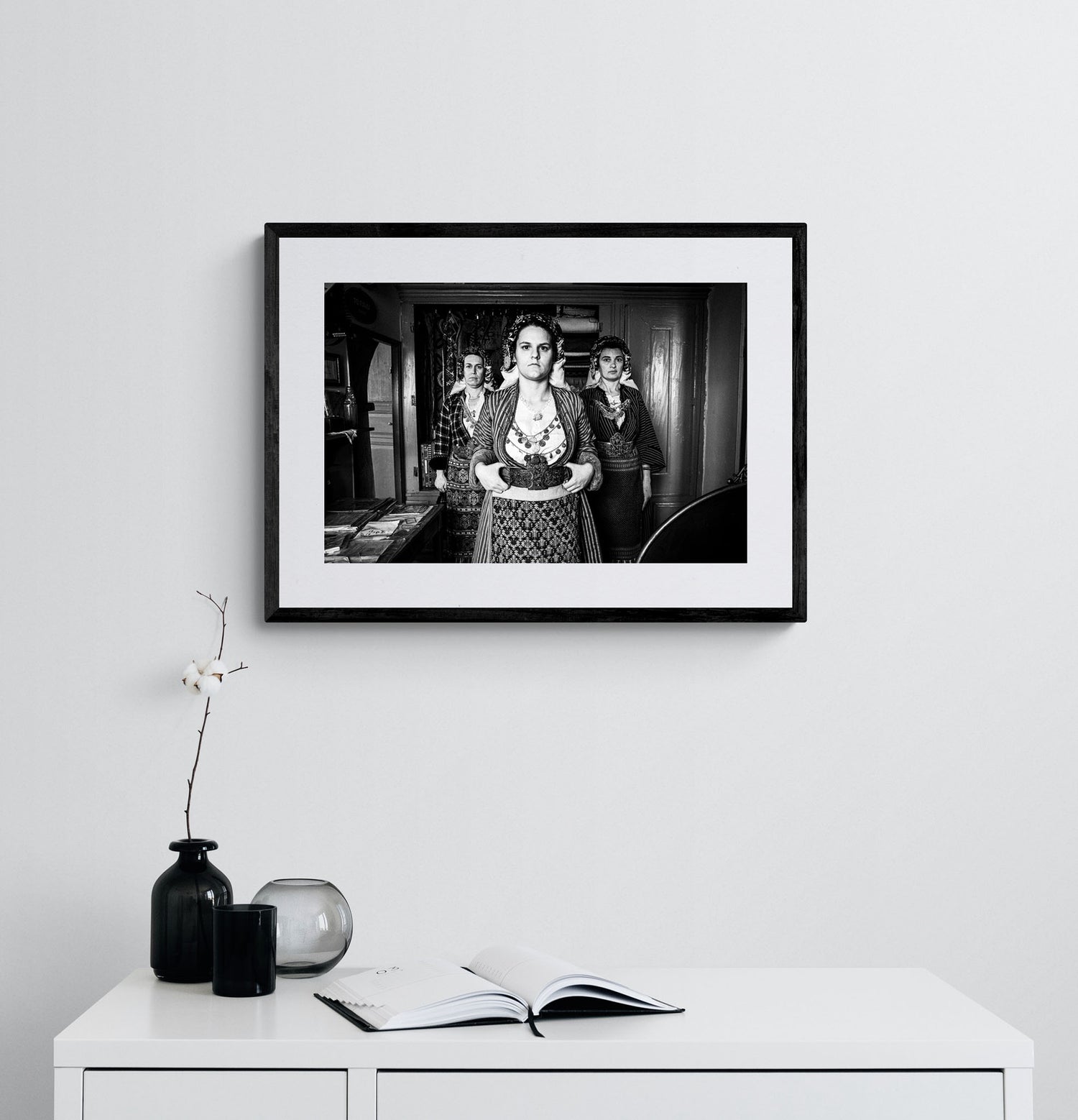 Black and white portrait of a woman in traditional attire with two other women in the background. Soufli local dresses, Thrace, Greece. Photography framed on a wall by George Tatakis