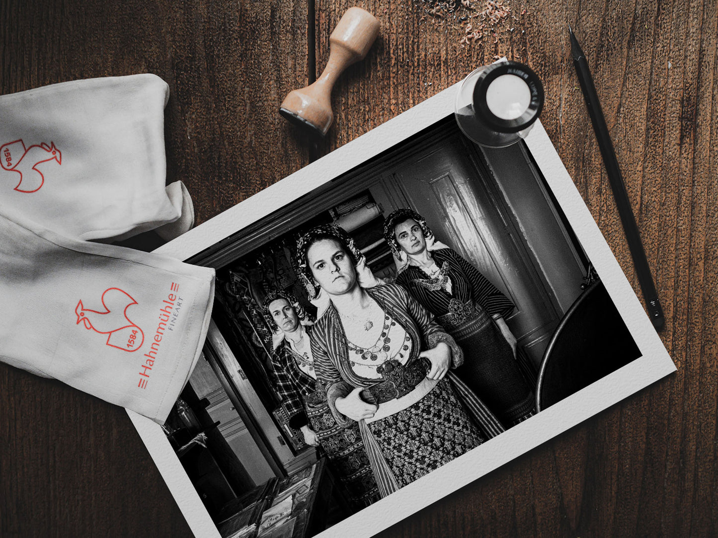 Black and white portrait of a woman in traditional attire with two other women in the background. Soufli local dresses, Thrace, Greece. Photography print on a table by George Tatakis