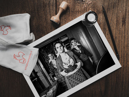 Black and white portrait of a woman in traditional attire with two other women in the background. Soufli local dresses, Thrace, Greece. Photography print on a table by George Tatakis
