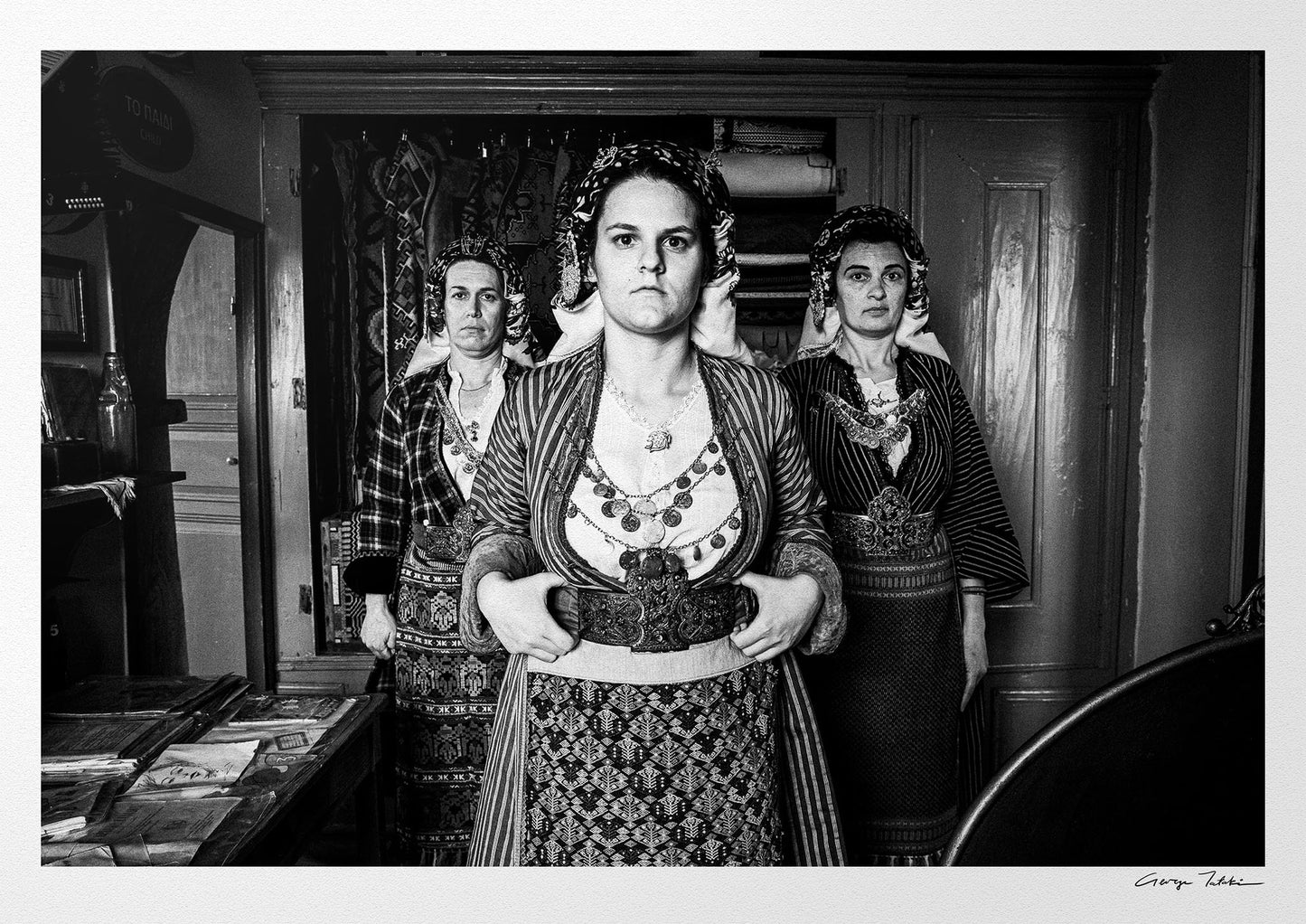 Black and white portrait of a woman in traditional attire with two other women in the background. Soufli local dresses, Thrace, Greece. Photography by George Tatakis