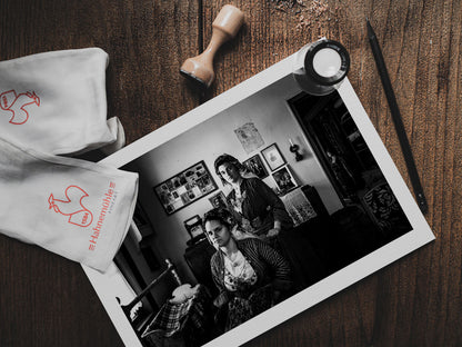 Two women in a room with framed pictures on the wall. Local dresses of Soufli, Thrace, Greece. Black and white photography pritn on table by George Tatakis.