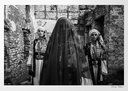 Three women in traditional attire standing in stone-walled ruins. Kyparissia, Peloponnese, Greece. Black and white photography by George Tatakis.